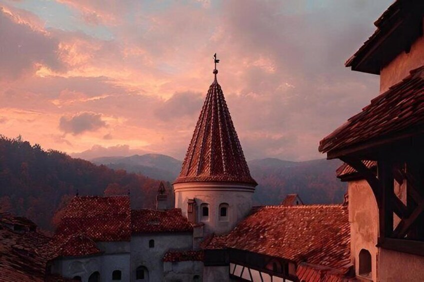 A church with a conical roof, surrounded by buildings with red-tiled roofs, under a sunset sky. 3