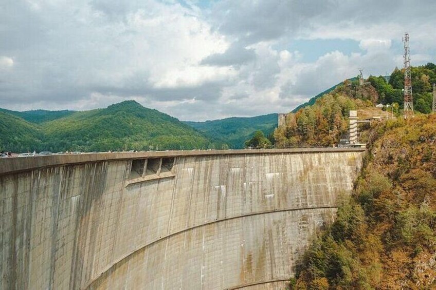A large concrete dam with a curved structure, surrounded by green hills and a cloudy sky. 5