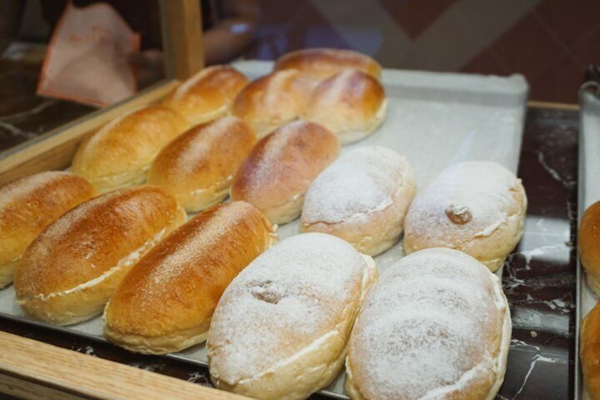 A display of various pastries, including bread rolls and doughnuts, dusted with powdered sugar. 3