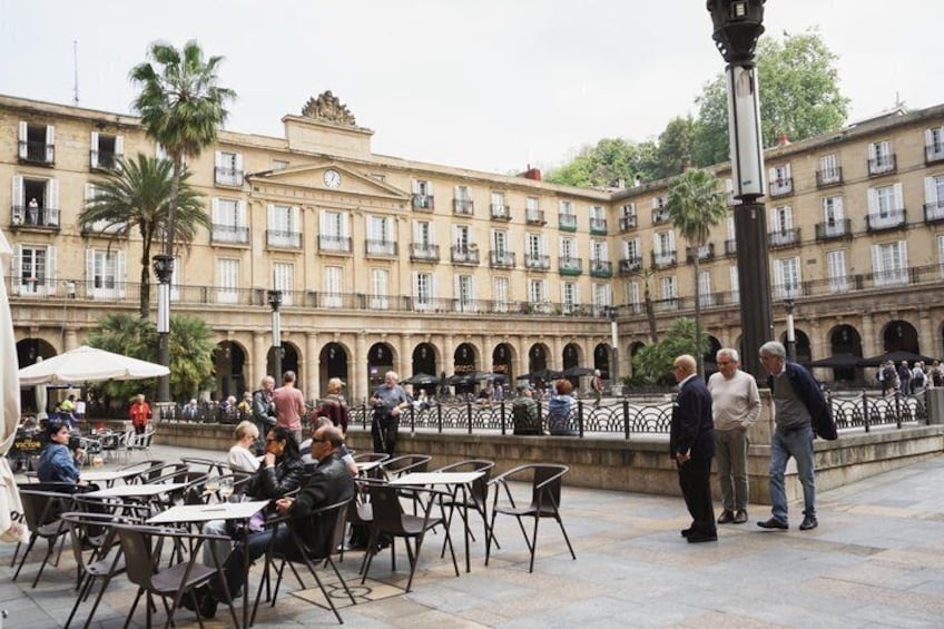 A courtyard with outdoor seating, palm trees, and historic buildings. 2