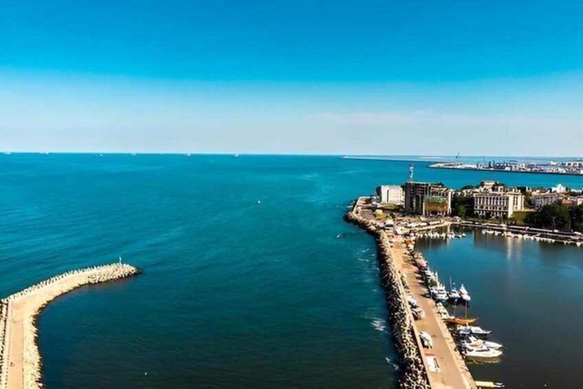 A coastal cityscape with a prominent breakwater, calm waters, and a clear sky. 5