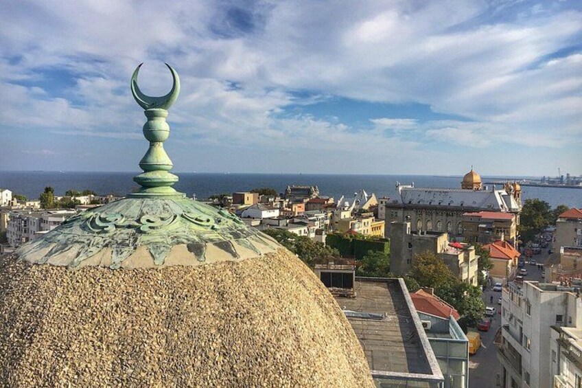 A domed building with a crescent moon finial, a golden dome, and a coastal cityscape in the background. 5