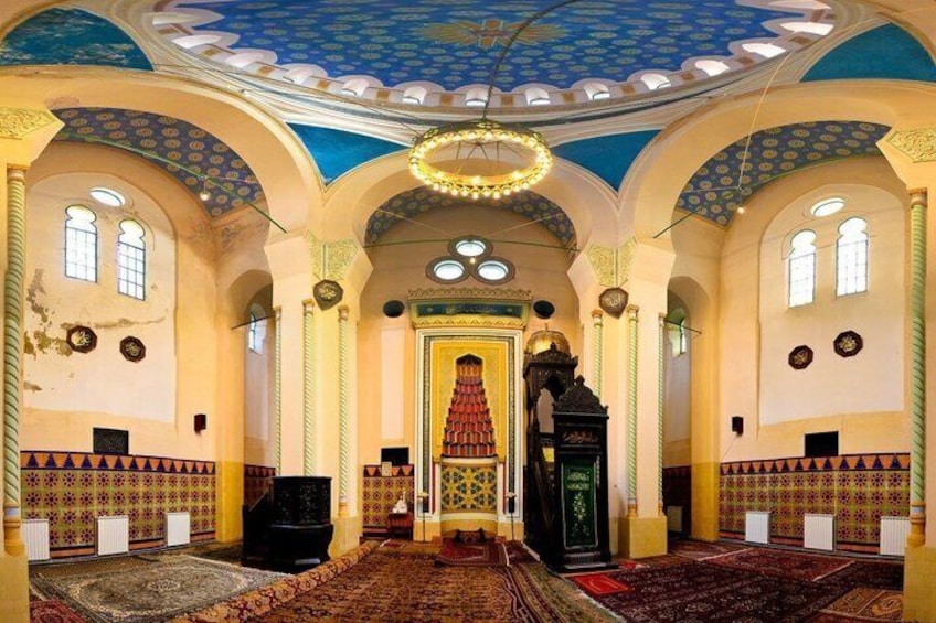 An interior of a mosque with a central prayer area, ornate arches, and a patterned ceiling. 2