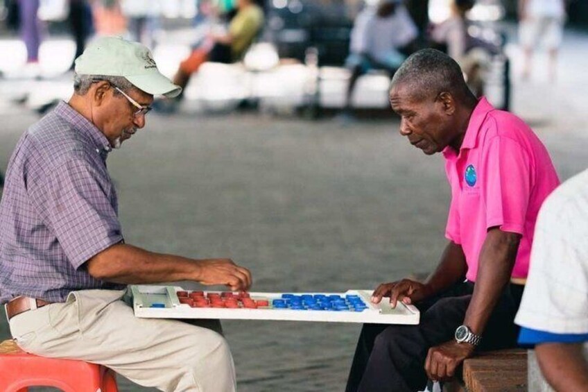 Two men sitting on a bench, one holding a board with colored blocks. 5
