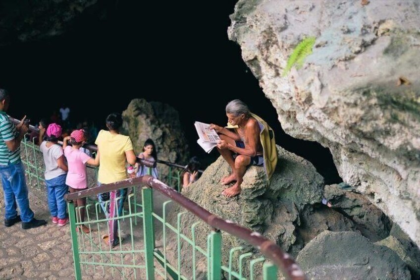 A cave entrance with visitors and a person reading a sign. 3