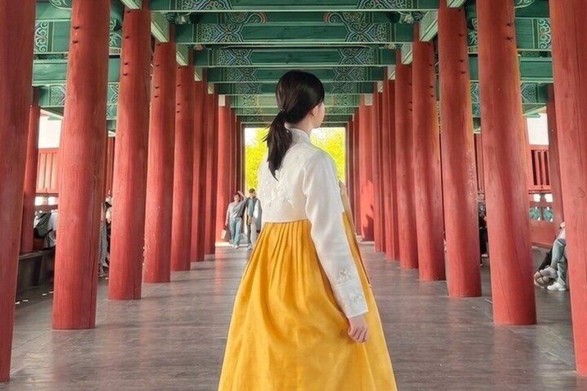 A person in traditional attire walking through a corridor with red pillars and green ceiling patterns. 5
