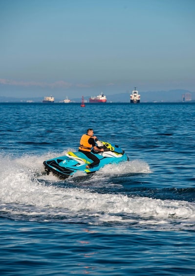 A person riding a jet ski on a body of water with ships in the distance. 1