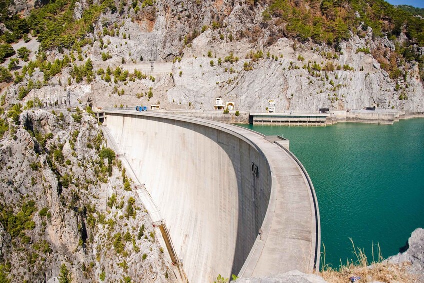 A large dam with a curved structure, a reservoir, and rocky terrain with sparse vegetation. 5