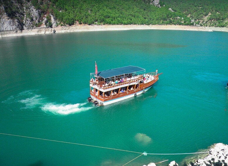A wooden boat with passengers, moving through turquoise waters near a rocky coastline. 4