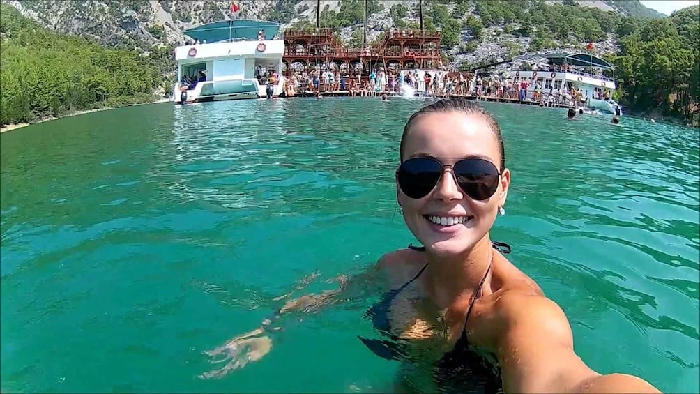 A person swimming in clear water with boats and a dock in the background. 2