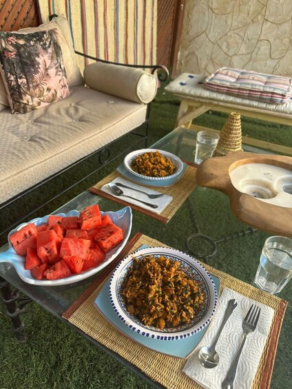 A glass table with a bowl of watermelon, a plate of rice, and a wooden bowl of soup. 5