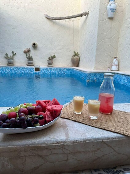 A poolside with a bowl of fruit, two drinks, and decorative pots. 4