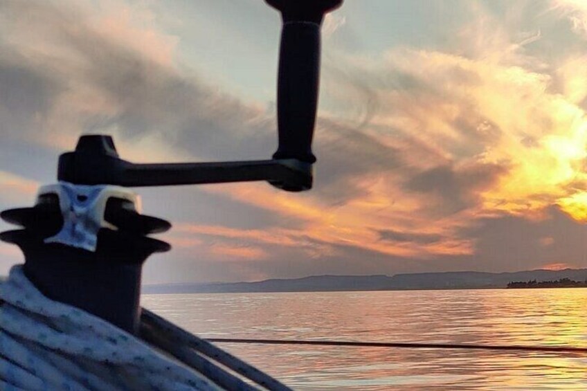 A boat's bow with a white sail and a black mast against a sunset sky. 2