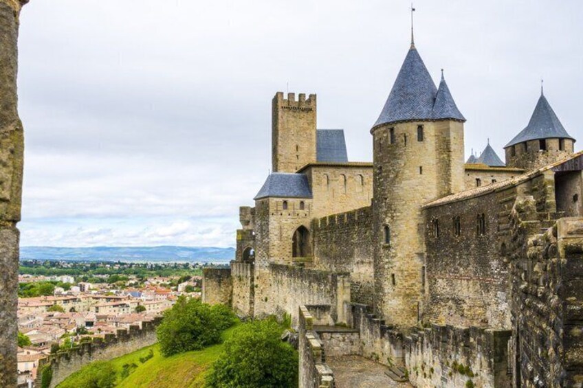 A historic stone castle with multiple towers and a fortified wall, overlooking a town below. 5