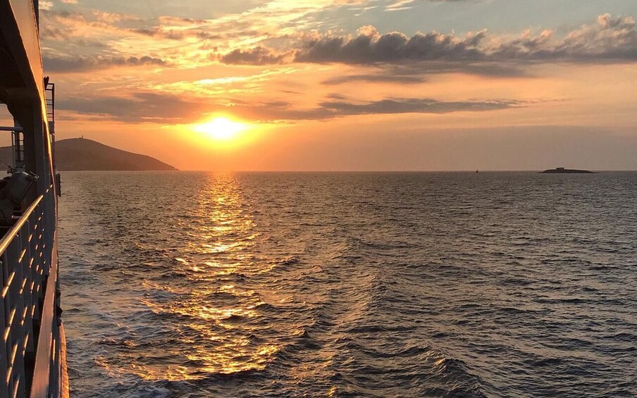 A sunset over the ocean with a ship's railing in the foreground. 4