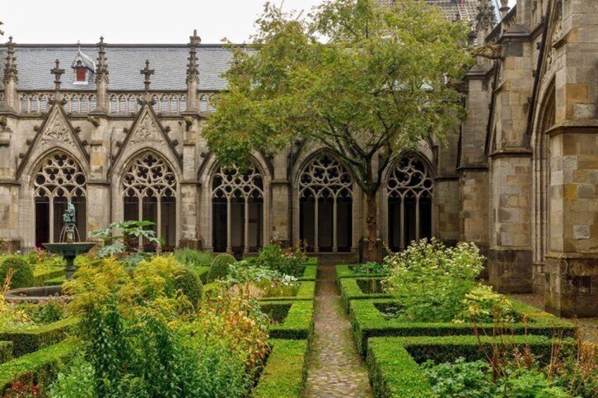A historic building with Gothic architecture, a formal garden with hedges, and a central pathway. 3