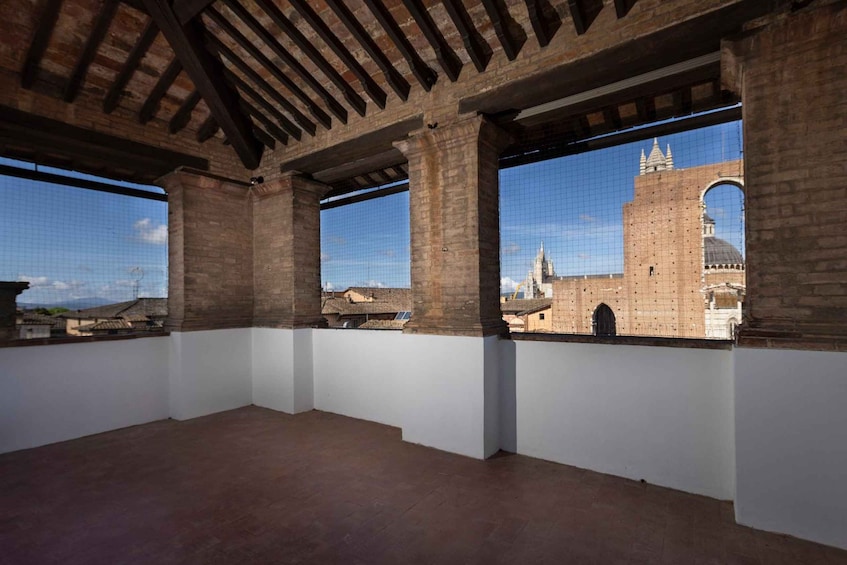 An interior space with brick walls and a tiled window overlooking a historic building with a dome. 2