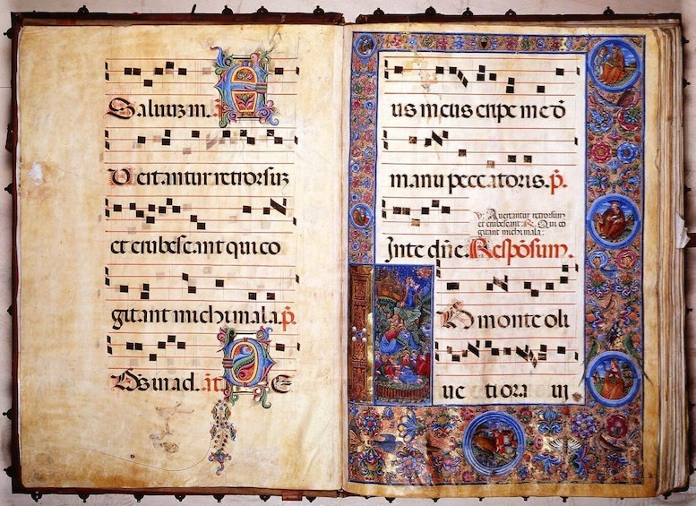 An open medieval manuscript with ornate decorations and musical notations. 3