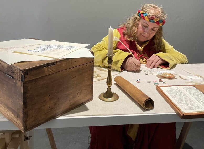 A person in historical attire working with documents and a wooden chest at a table. 5