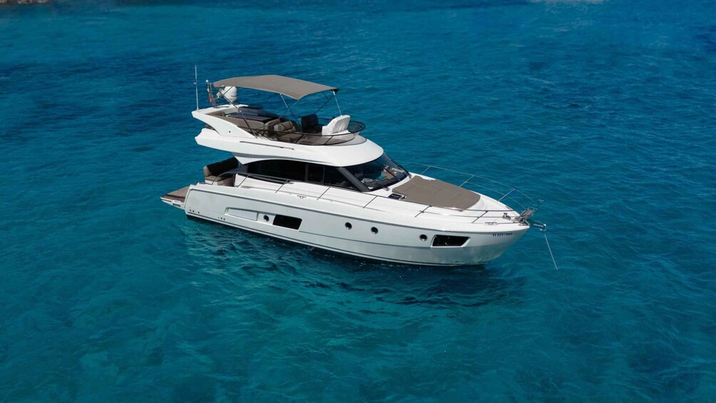 A white yacht with a covered upper deck and a cabin, floating on clear blue water. 1