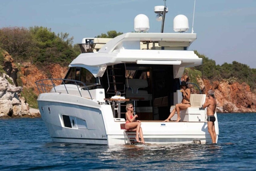 A white yacht with two people on the deck, one sitting and one standing, in calm waters with a rocky coastline in the background. 5