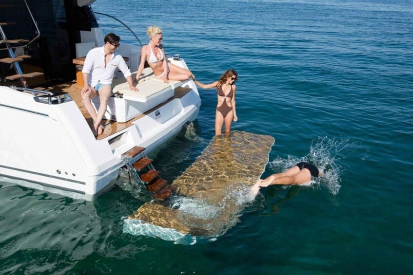 A yacht with a flat deck extending into the water, a person swimming, and another person standing on the deck. 5