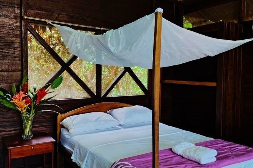 A wooden bed with a white canopy, a bedside table with a vase of flowers, and a pink blanket. 2