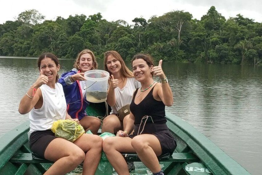 Four people on a green boat with a forested lake in the background. 4