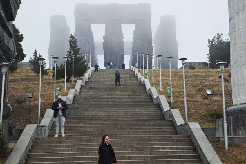 A person descending a set of stairs towards a large stone archway. 3