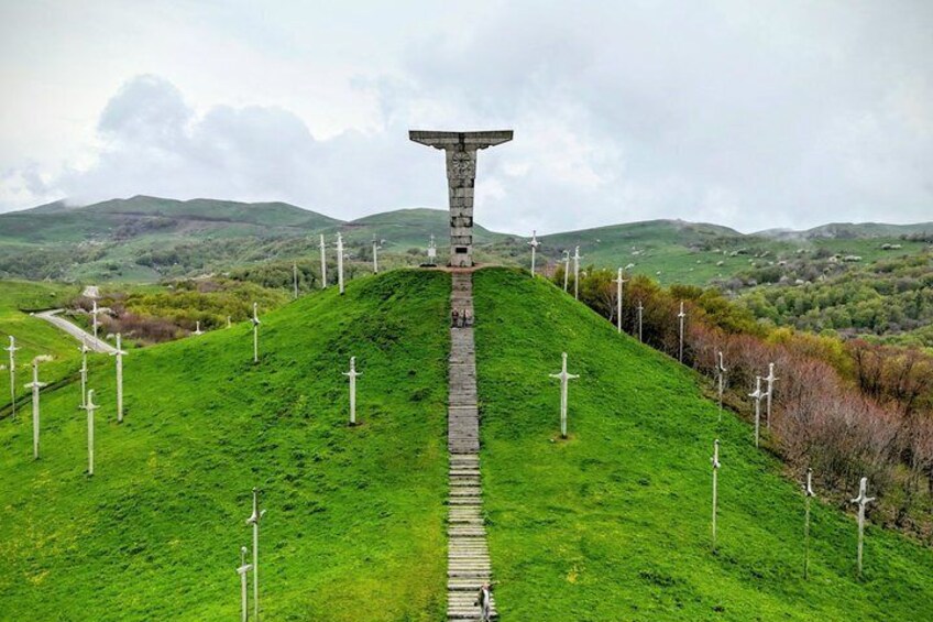 A stone monument on a grassy hill with multiple crosses in the background. 1