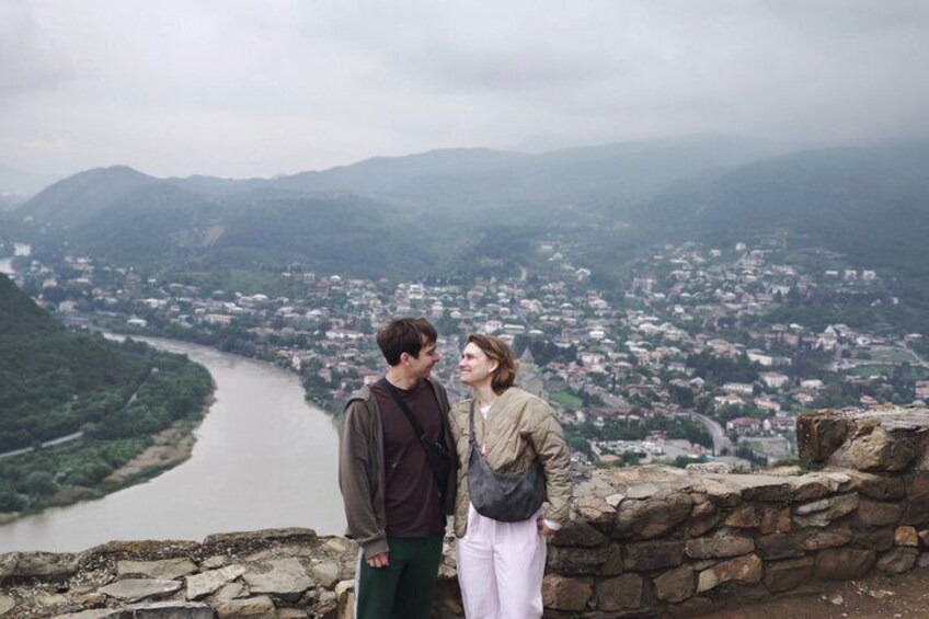 Two people standing on a stone wall overlooking a river and a town. 5