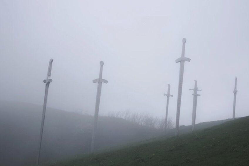 A misty landscape with several swords standing upright on a grassy hill. 2