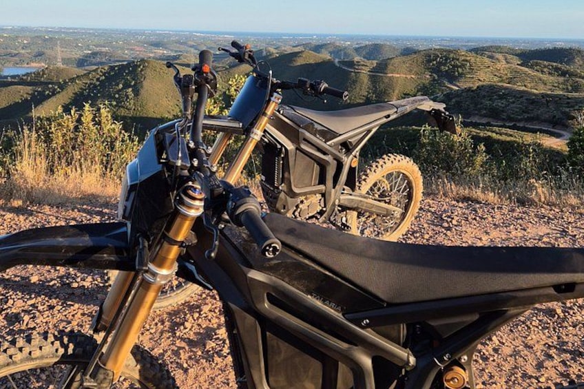 A dirt bike parked on a rocky terrain with a scenic view of hills and a lake in the distance. 2