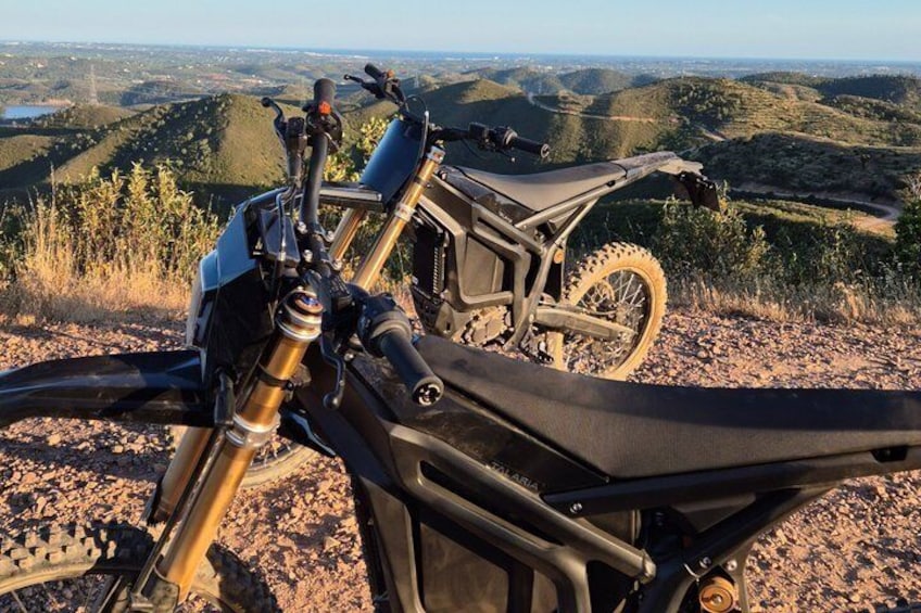 A dirt bike parked on a rocky terrain with a scenic view of hills and a clear sky. 2