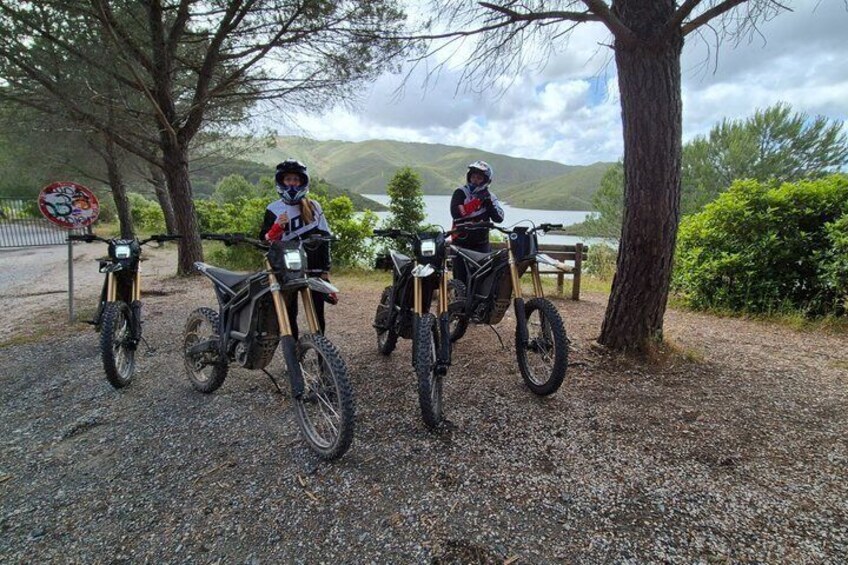 Three off-road motorcycles parked on a gravel path with a lake and hills in the background. 5