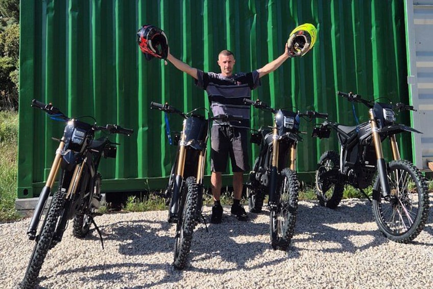 A person standing between three dirt bikes in front of a green shipping container. 3