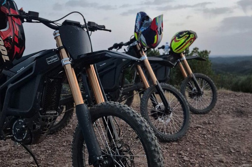 A dirt bike and a mountain bike on a dirt trail with helmets and a backpack. 5