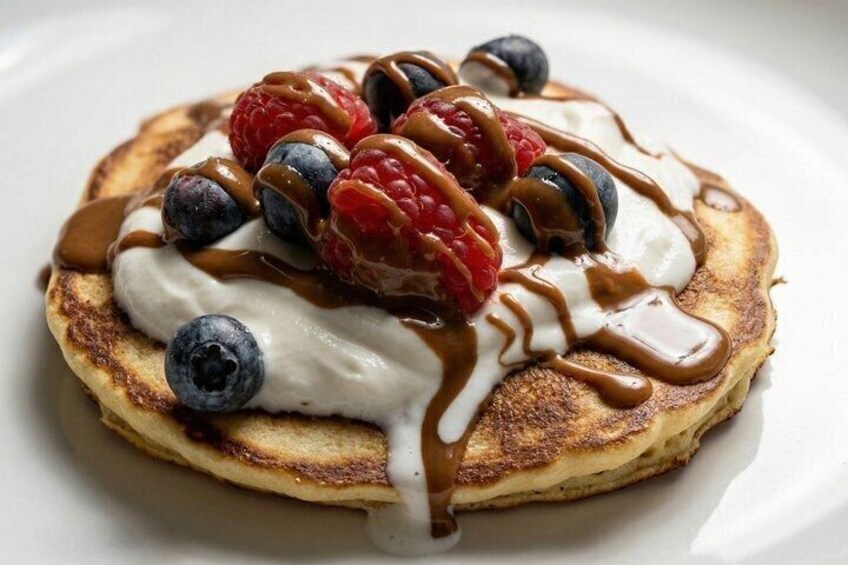 A stack of pancakes topped with whipped cream, blueberries, raspberries, and a drizzle of syrup. 4