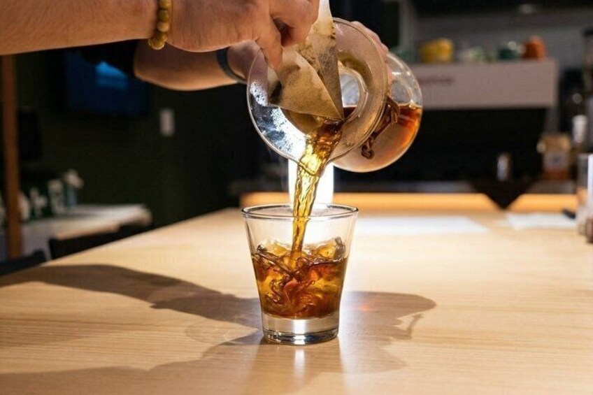 A hand pouring a dark liquid into a glass with ice cubes. 3