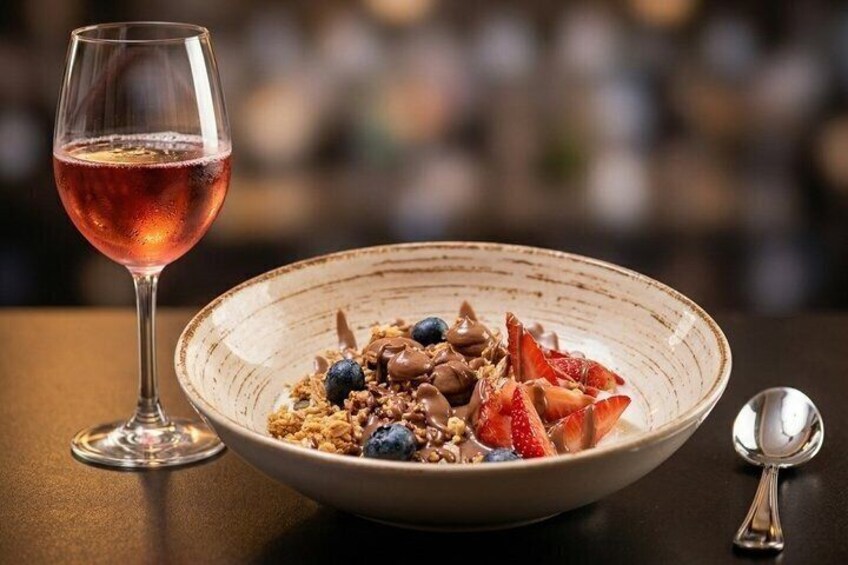 A bowl of cereal with strawberries and blueberries, a glass of pink drink, and a spoon on a table. 5