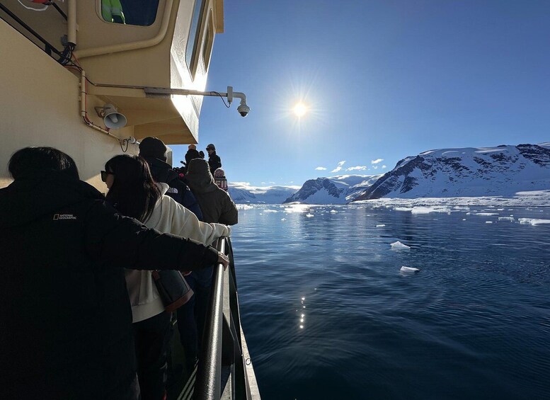 A group of people on a boat observing icebergs and mountains in a clear, sunny day. 2