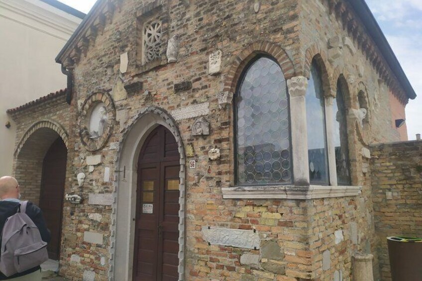 A historic stone building with arched windows and a door, featuring decorative elements and inscriptions. 3