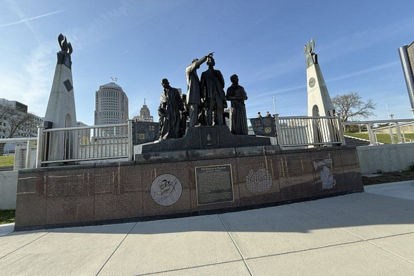 A statue of historical figures on a pedestal with a cityscape in the background. 4