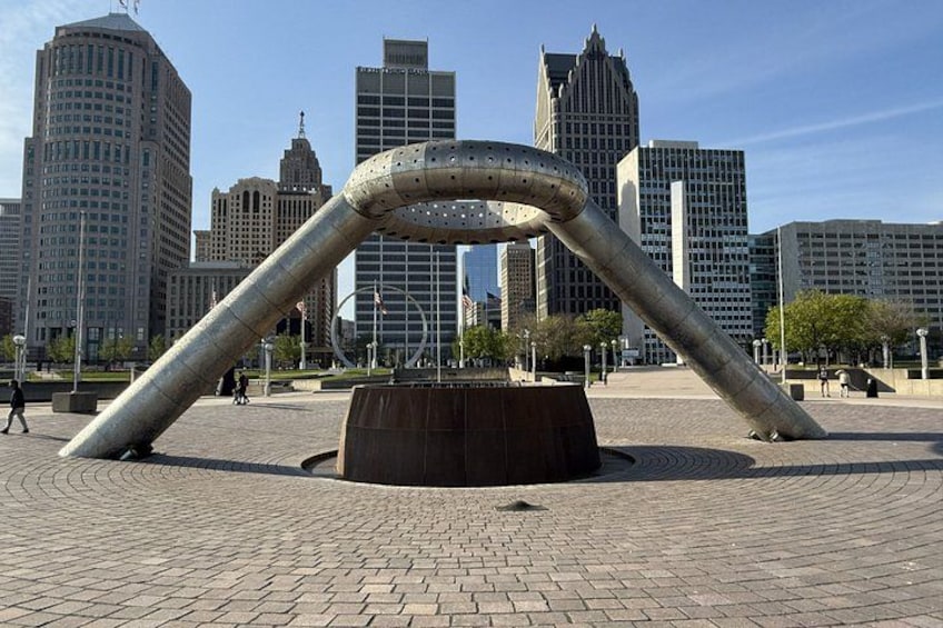 A large metallic sculpture in an urban plaza with modern buildings in the background. 2