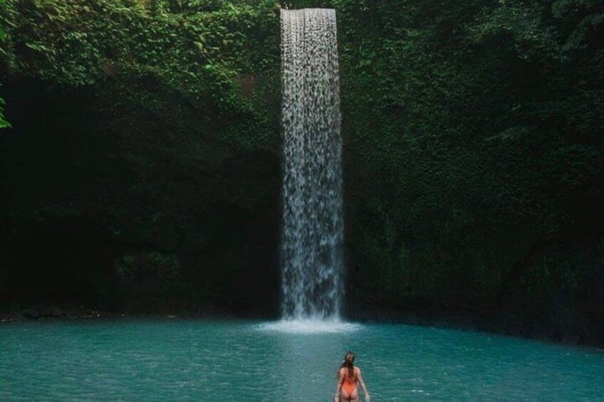 A waterfall in a forested area with a person standing in the water. 3