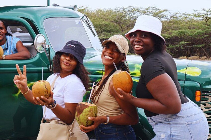Three people holding coconuts, standing next to a green truck. 4