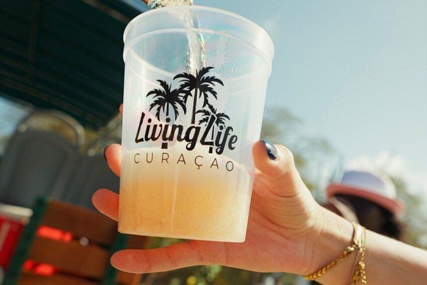 A hand holding a clear plastic cup with a straw, labeled 'Living Life CURACAO.' 2