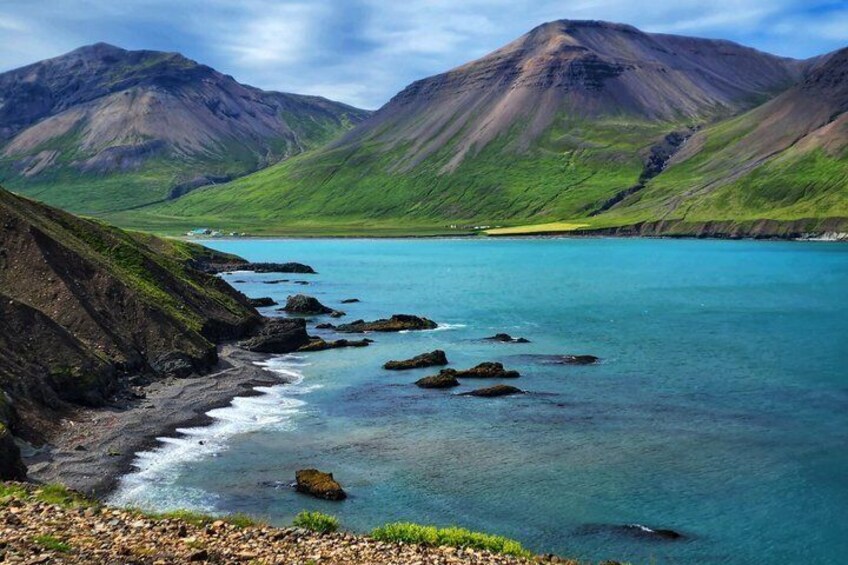 A coastal landscape with a clear turquoise sea, rocky shoreline, and green hills. 1