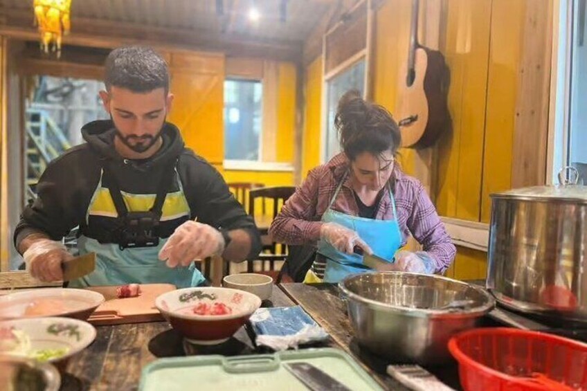 Two people cooking in a kitchen with wooden walls and a guitar in the background. 5