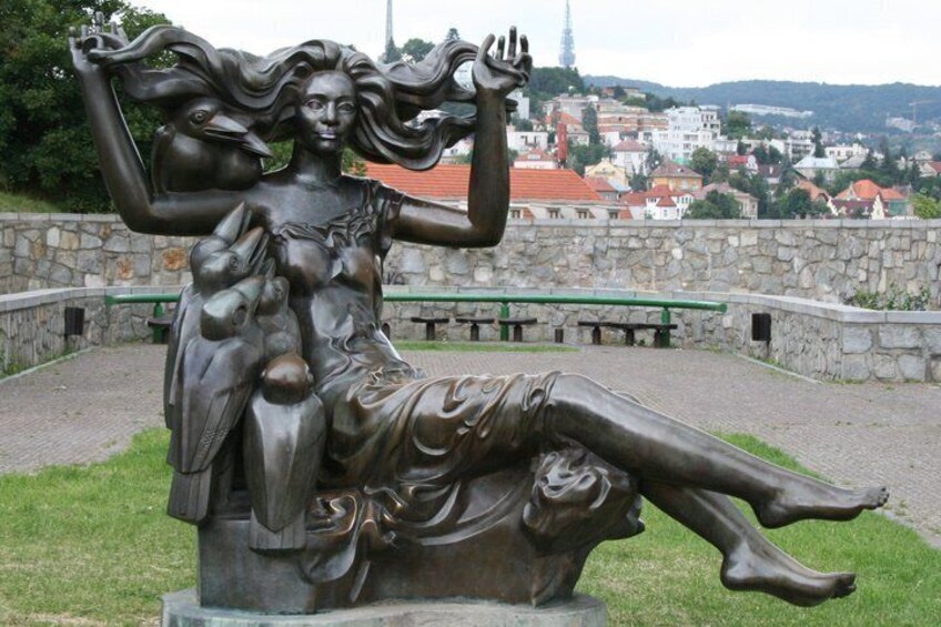 A bronze statue of a woman holding a child, with a stone wall and benches in the background. 5